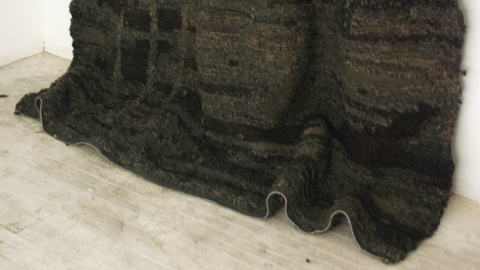 A large, dark weaving hanging on a wall